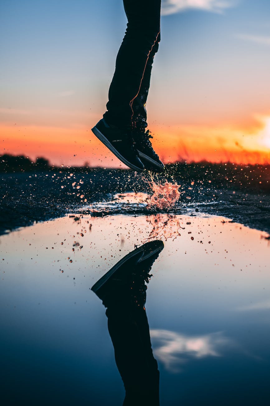 reflection photo of person jumping on water puddle